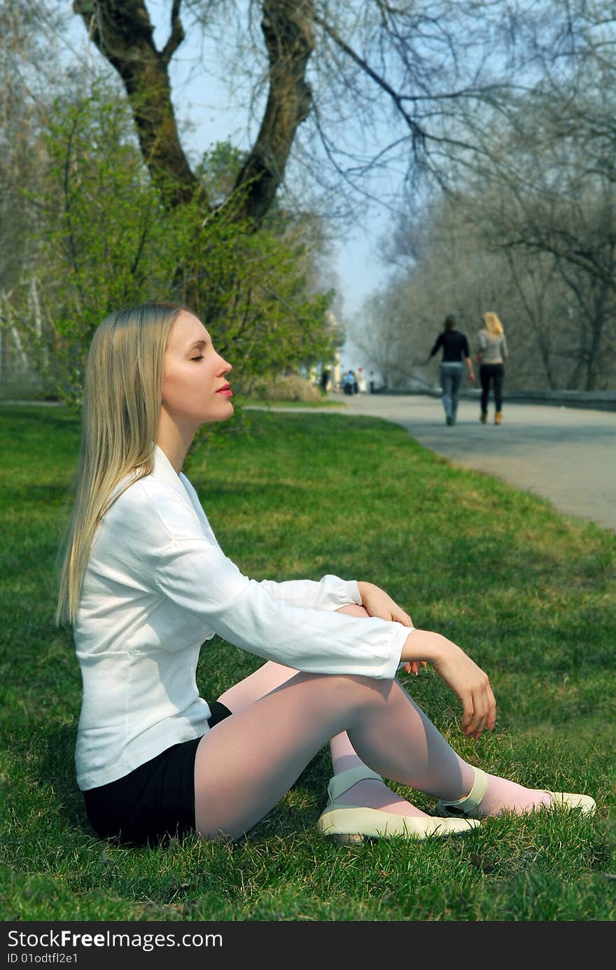 The woman sitting on a grass in park in a white blouse