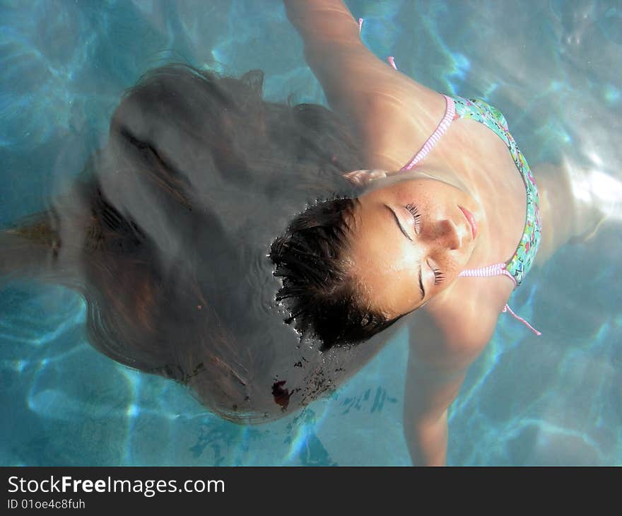 A young brown haired girl in a tropical swimming pool, floating in the water. A young brown haired girl in a tropical swimming pool, floating in the water.