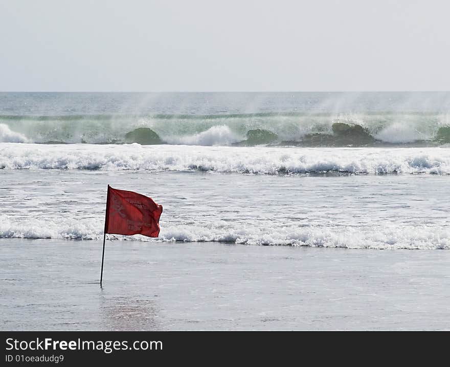Red warning flag standing against big ocean waves. Bali, Kuta beach.