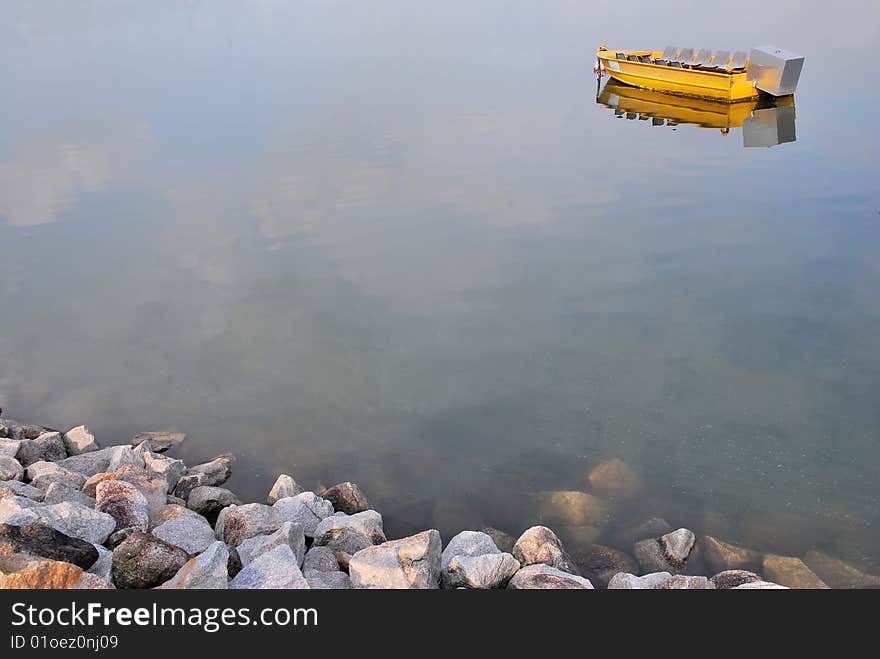 Isolated yellow boat with jugged rocks in the foreground. Isolated yellow boat with jugged rocks in the foreground