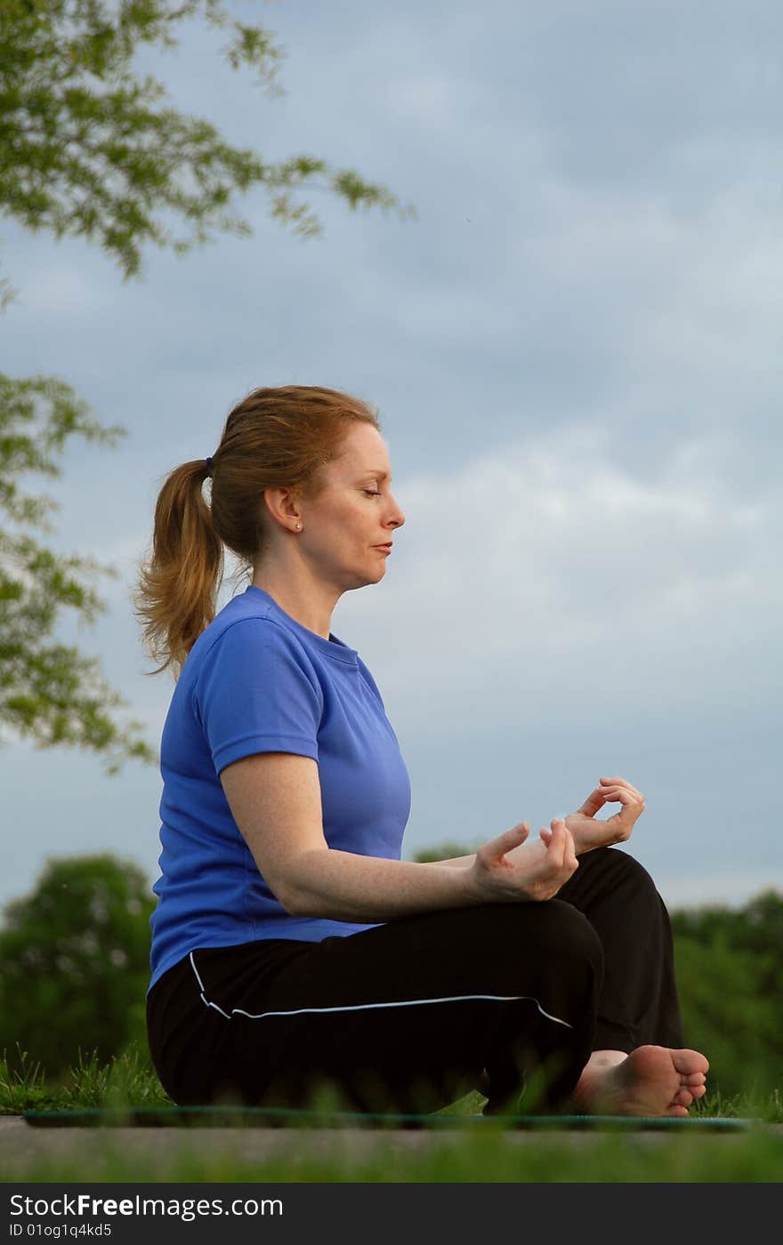 A woman sits in a lotus pose meditating with blue sky. A woman sits in a lotus pose meditating with blue sky