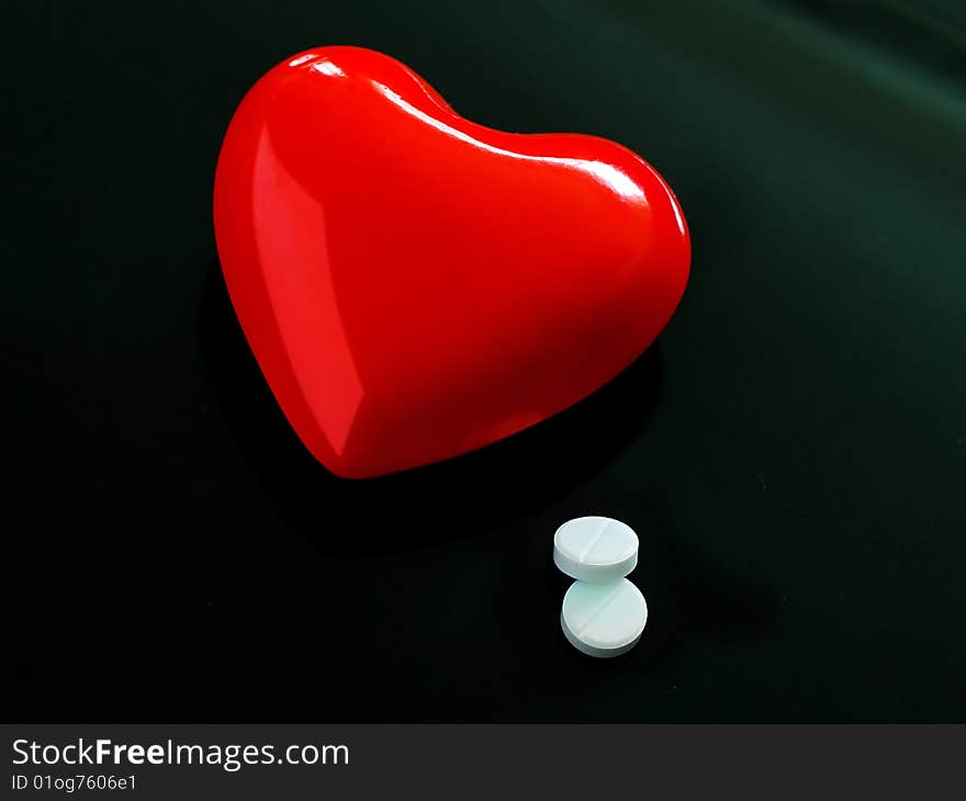 A red heart on black background lies near pills a concept for medicne