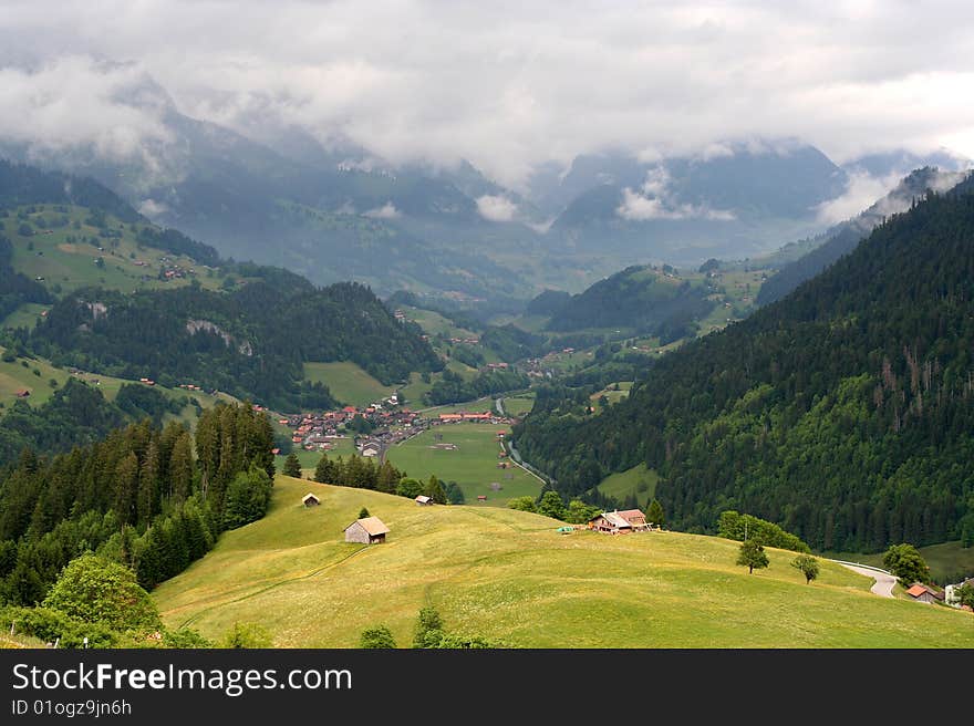 A mountain village in Switzerland, laying in a valley with could covered mountains in the background. A mountain village in Switzerland, laying in a valley with could covered mountains in the background