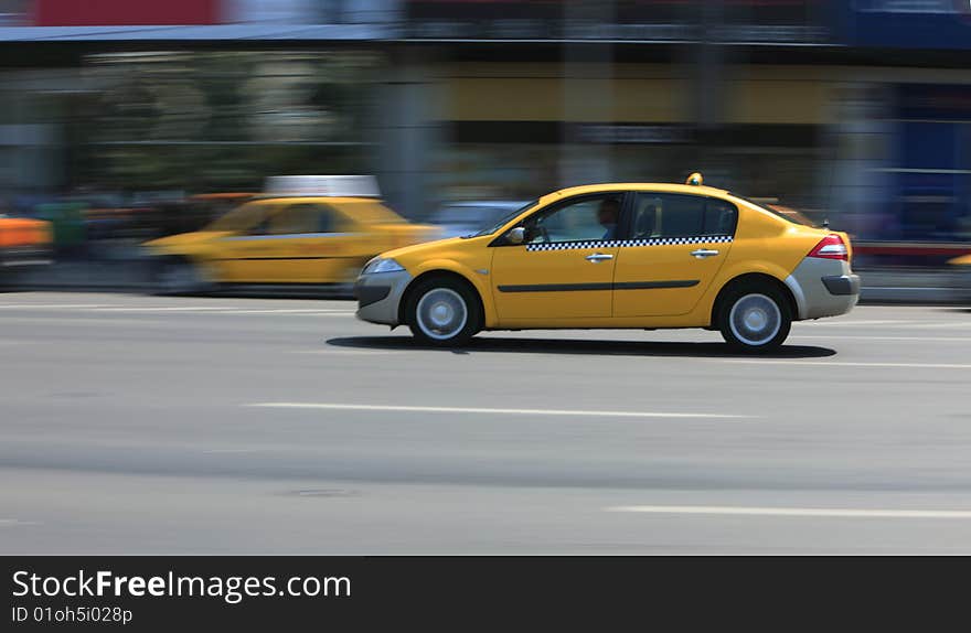 Panning image of a yellow cab in a city street.