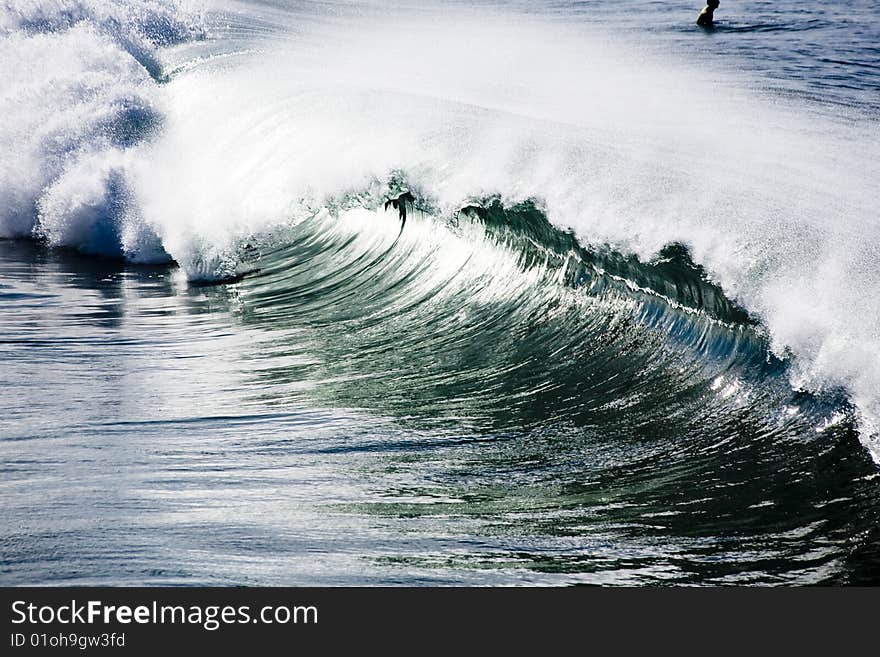 Barreling wave crashing on the beach with surfer in background. Barreling wave crashing on the beach with surfer in background