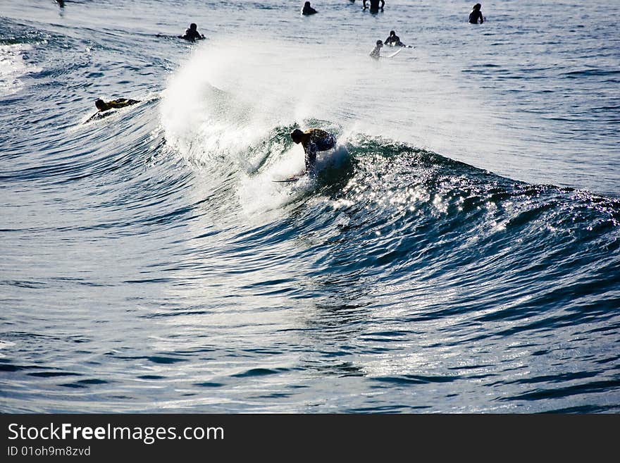 Surfer dropping in on a nice clean wave. Croud of surfers in the background.