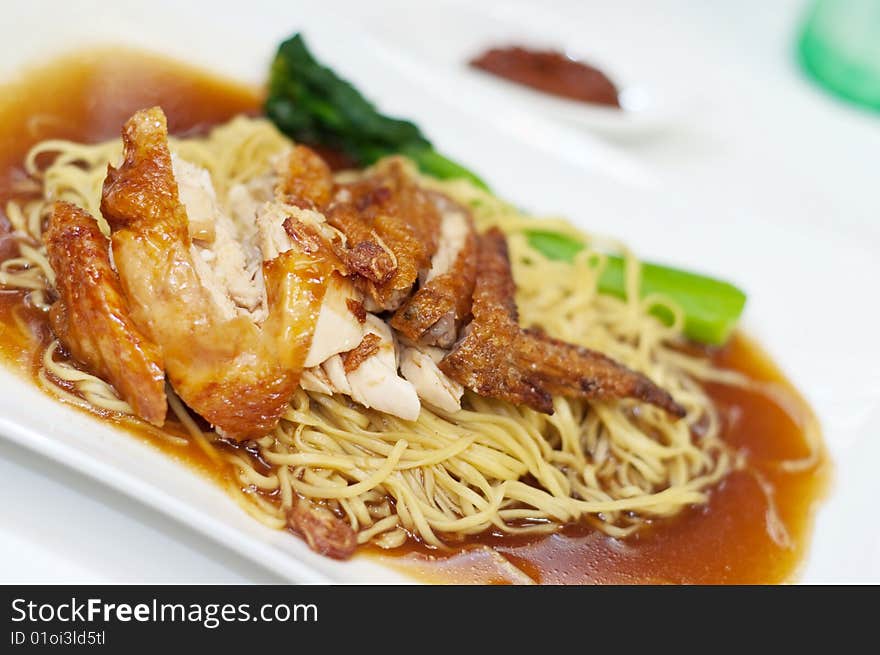 A plate of delicious chicken wing noodles, topped with mouth watering gravy sauce and complete with a tinge of vegetable stalk by the side, a delicacy in Asian countries. A plate of delicious chicken wing noodles, topped with mouth watering gravy sauce and complete with a tinge of vegetable stalk by the side, a delicacy in Asian countries.