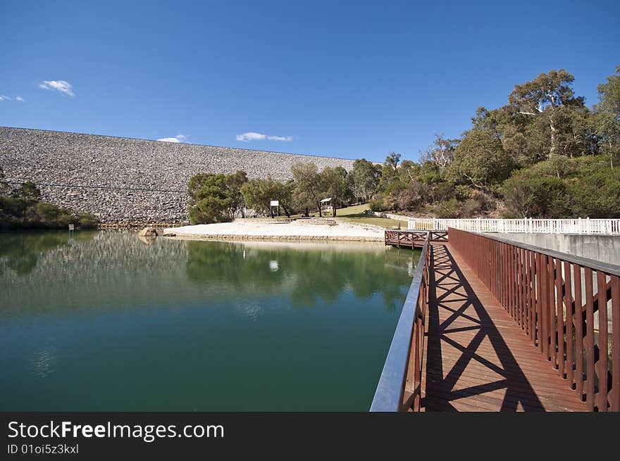 A wooden bridge beside a beautiful clear crystal lake, surrounded by vegetations and against the blue sky. A wooden bridge beside a beautiful clear crystal lake, surrounded by vegetations and against the blue sky.