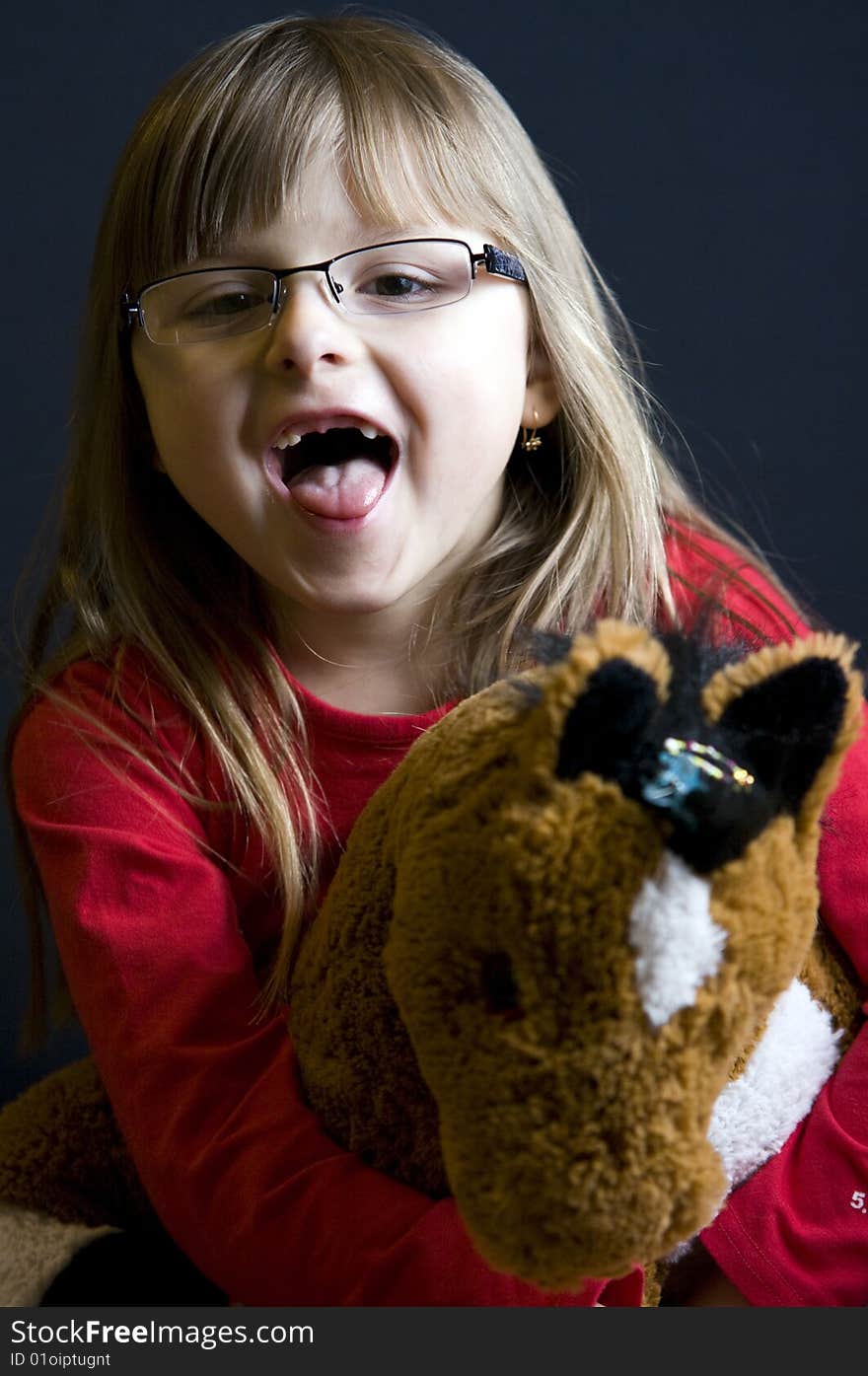 A young blonde girl playing with her soft toy horse, making a funny face, her front teeth missing. A young blonde girl playing with her soft toy horse, making a funny face, her front teeth missing.