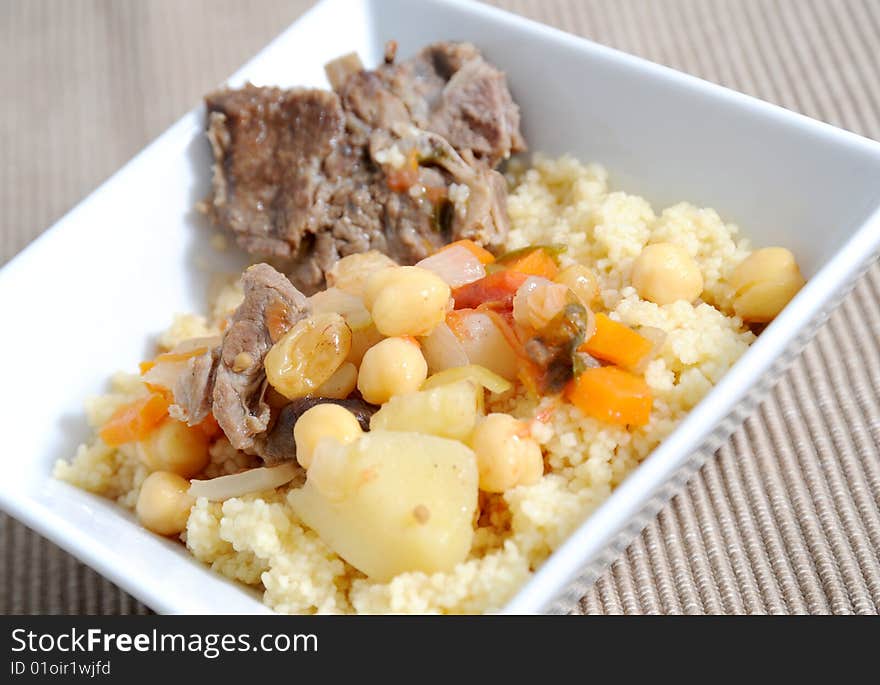 Sticky lamb with couscous, garnished with spring potatoes carrots and chickpeas