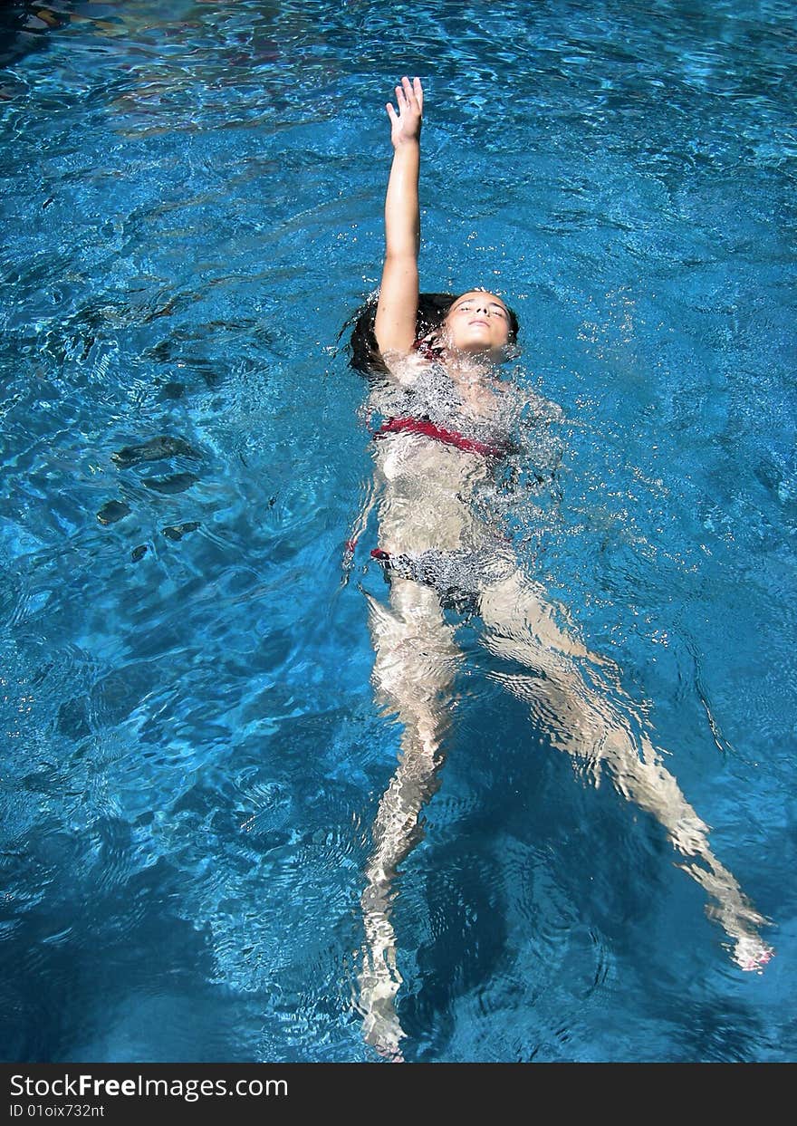 A girl in a bikini swimming the backstroke in a tropical pool. A girl in a bikini swimming the backstroke in a tropical pool.