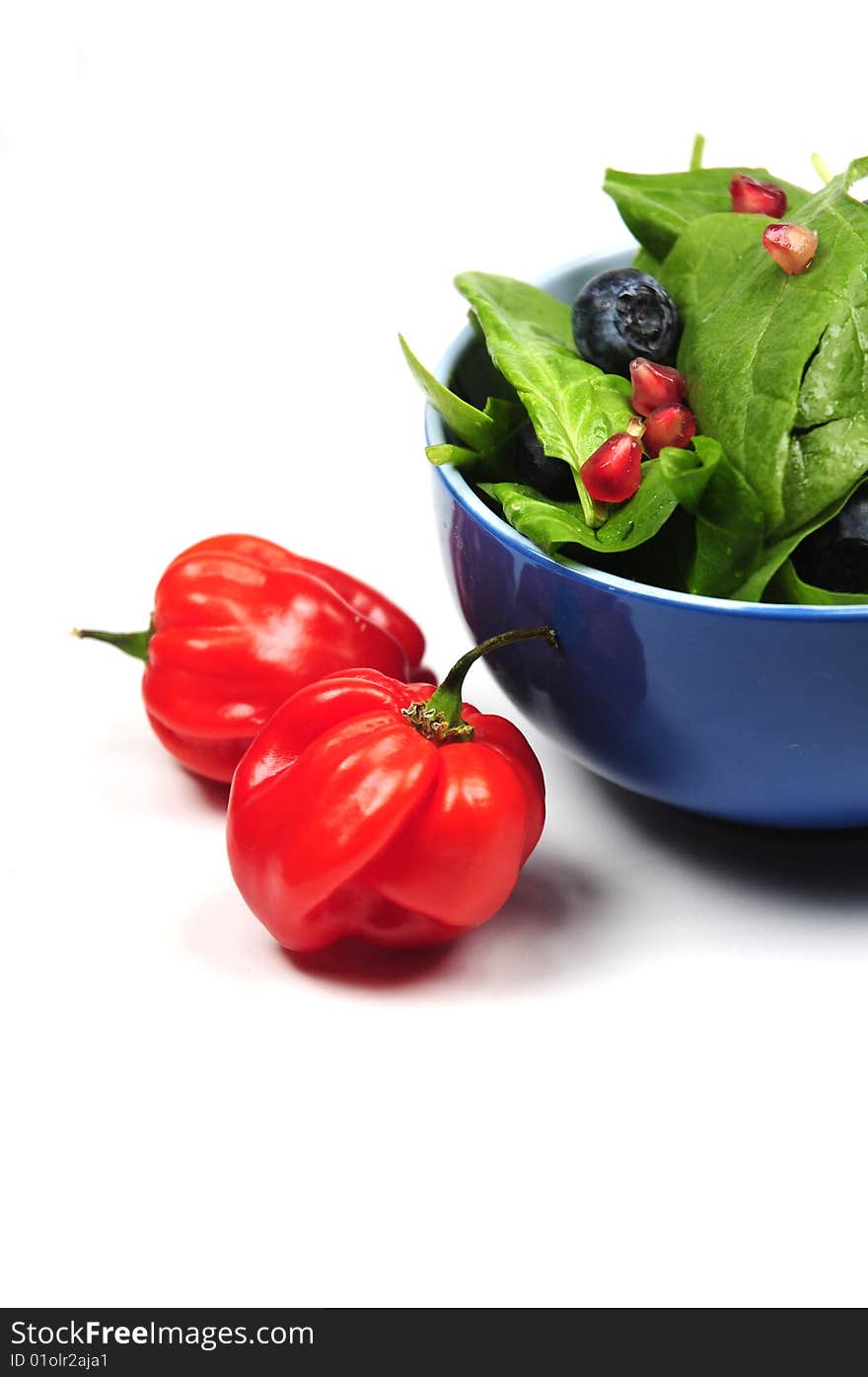 Two ripe and red peppers next to a bowl of fresh salad. Two ripe and red peppers next to a bowl of fresh salad.