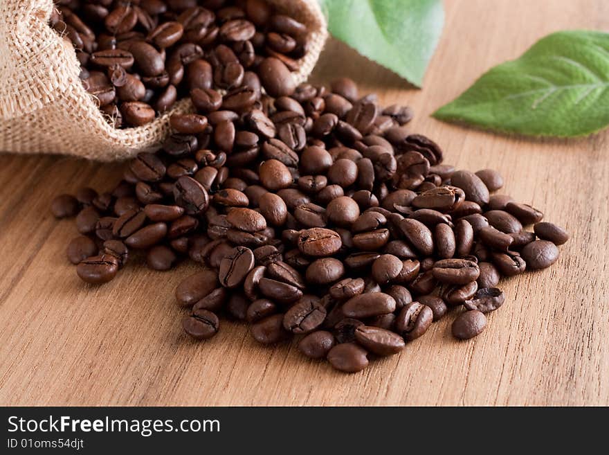 A bunch of coffee beans, falling out of a sack on a wooden background