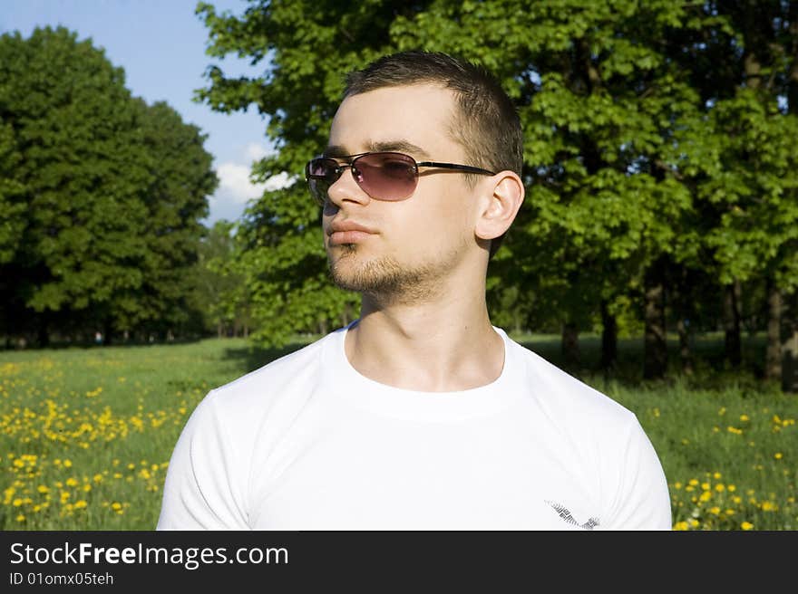 The young man costs in park. On eyes glasses. In white vest. The young man costs in park. On eyes glasses. In white vest