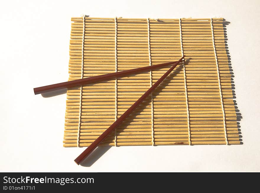 A Pair or square wooden chopsticks on a bamboo maki rolling mat on a white background. A Pair or square wooden chopsticks on a bamboo maki rolling mat on a white background