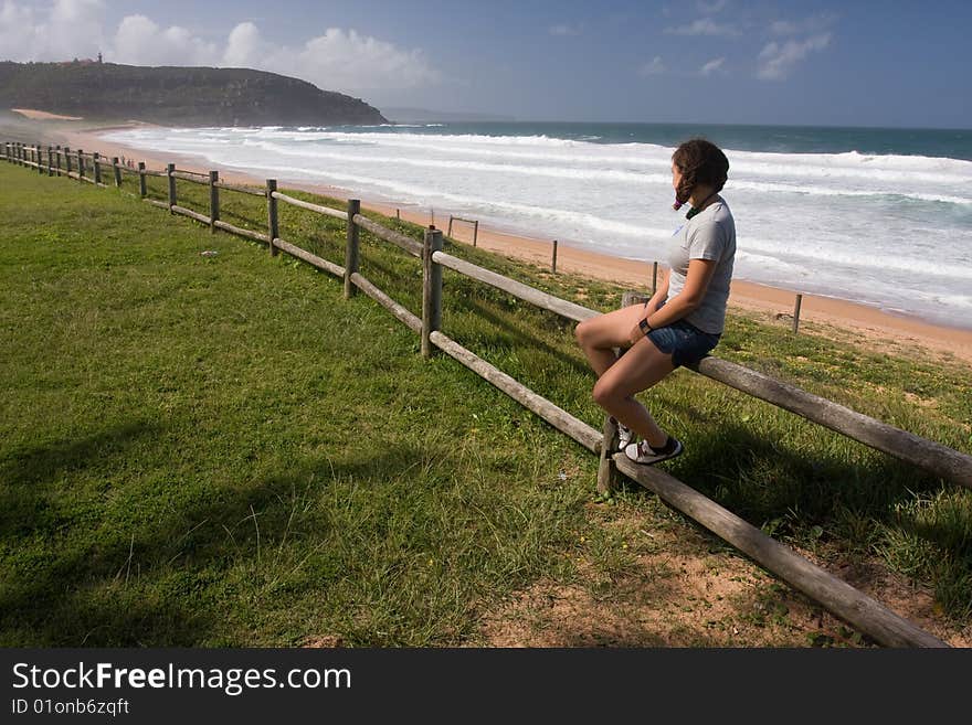 Young girl is siiting on the beach fence and watching the ocean. Young girl is siiting on the beach fence and watching the ocean.