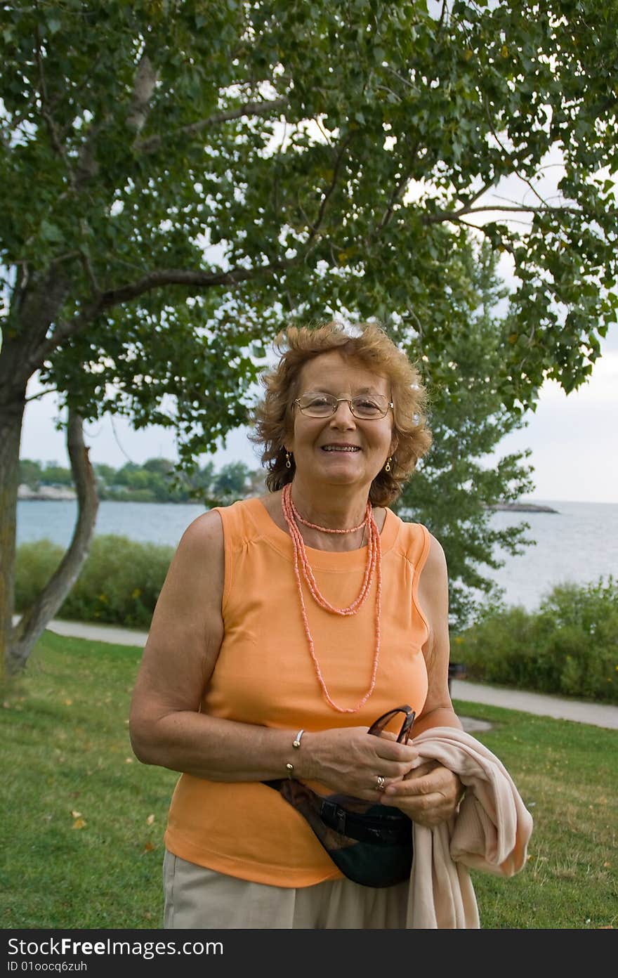 Smiling older lady walking outdoor by a lake. Smiling older lady walking outdoor by a lake