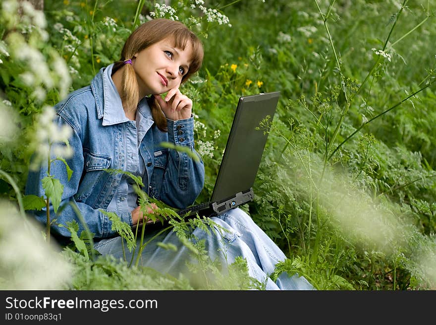 The beautiful girl with the laptop in park sits in a green grass. The beautiful girl with the laptop in park sits in a green grass