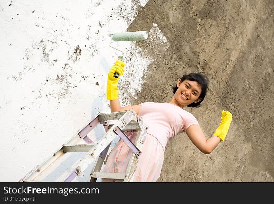 Cheerful asian woman showing her strength, capacity and capability. painting exterior wall of her house by herself with a white colored paint, using a ladder, roller and gloves on hands. Cheerful asian woman showing her strength, capacity and capability. painting exterior wall of her house by herself with a white colored paint, using a ladder, roller and gloves on hands