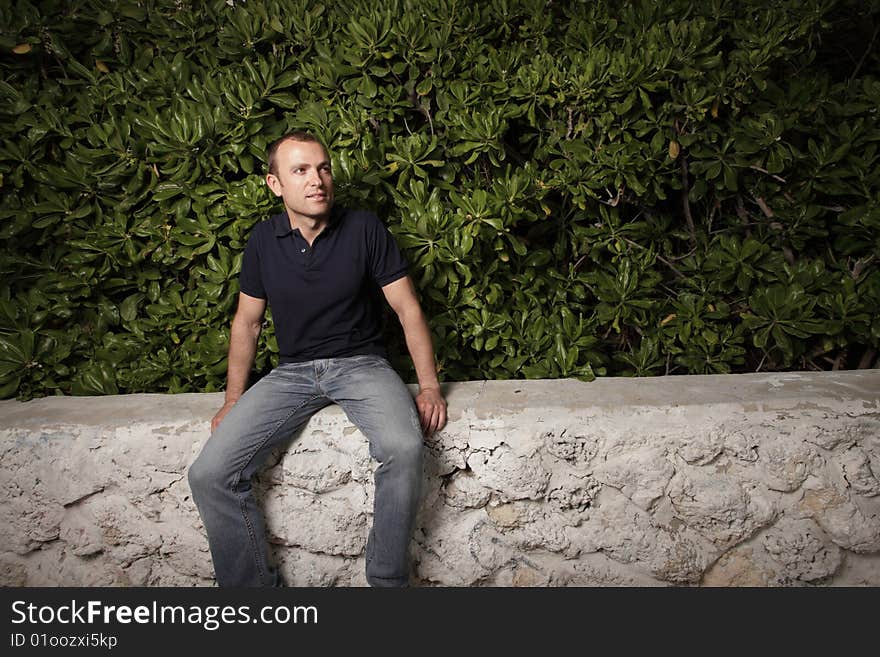 Young man sitting on a ledge by bushes