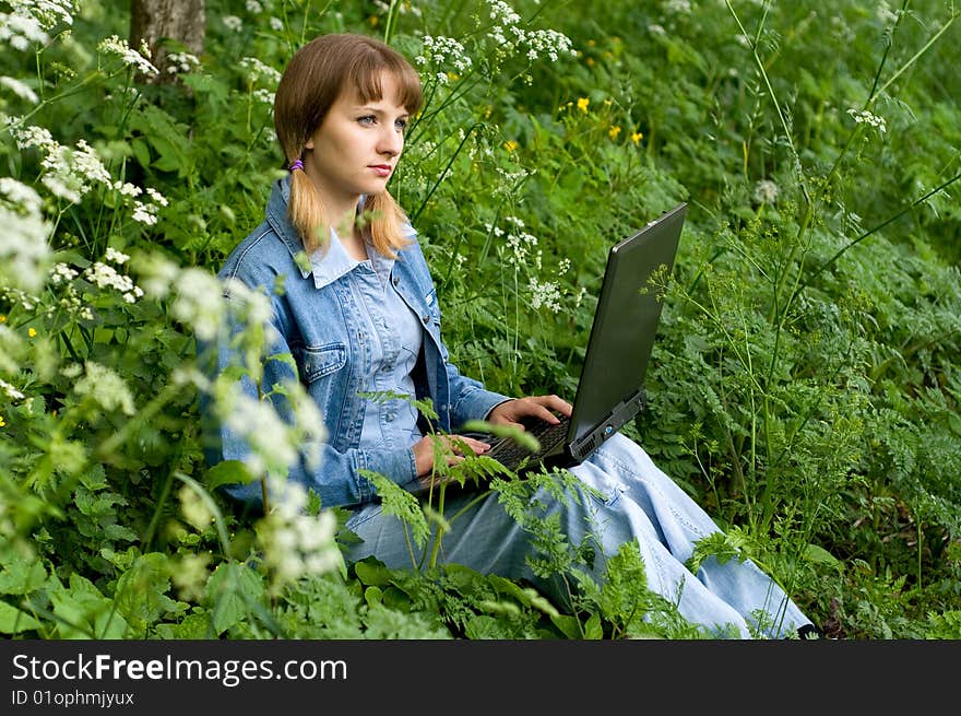 The beautiful girl with the laptop in park sits in a green grass. The beautiful girl with the laptop in park sits in a green grass