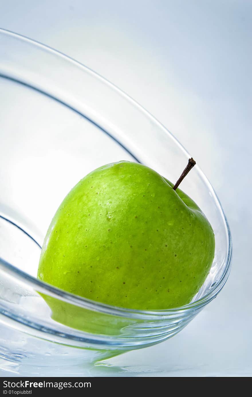 Green apple in glass plate on blue background