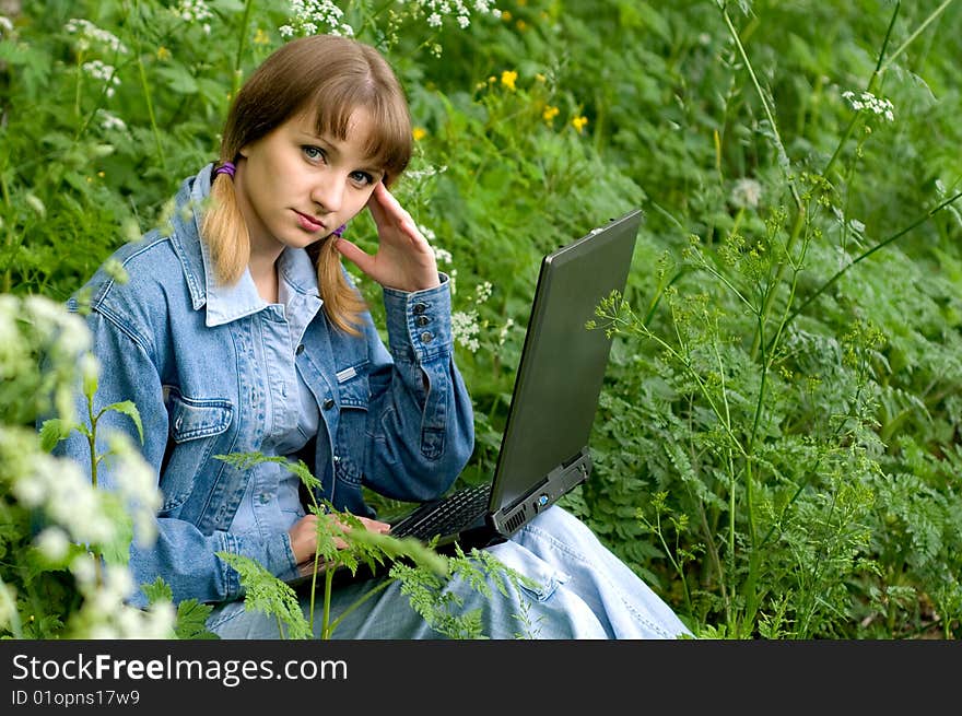 The beautiful girl with the laptop in park sits in a green grass. The beautiful girl with the laptop in park sits in a green grass