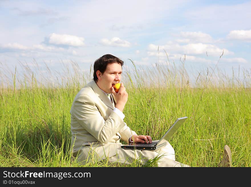 Businessman with laptop siting on green grass, eating apple, relaxing. Businessman with laptop siting on green grass, eating apple, relaxing