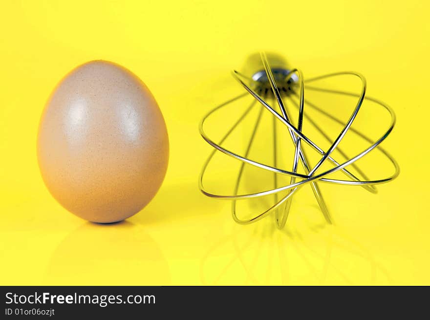 An egg and and a egg beater together isolated against a yellow background