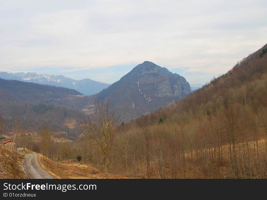 Italy. The Alpes. Early spring. Still there is no green grass. On trees there is no foliage. At mountain tops the snow has not thawn. The nature waits for present heat. Cloudy day. A kind on a valley, mountains from a slope of a hill. At the left – the road going downwards, country economic construction. Italy. The Alpes. Early spring. Still there is no green grass. On trees there is no foliage. At mountain tops the snow has not thawn. The nature waits for present heat. Cloudy day. A kind on a valley, mountains from a slope of a hill. At the left – the road going downwards, country economic construction.