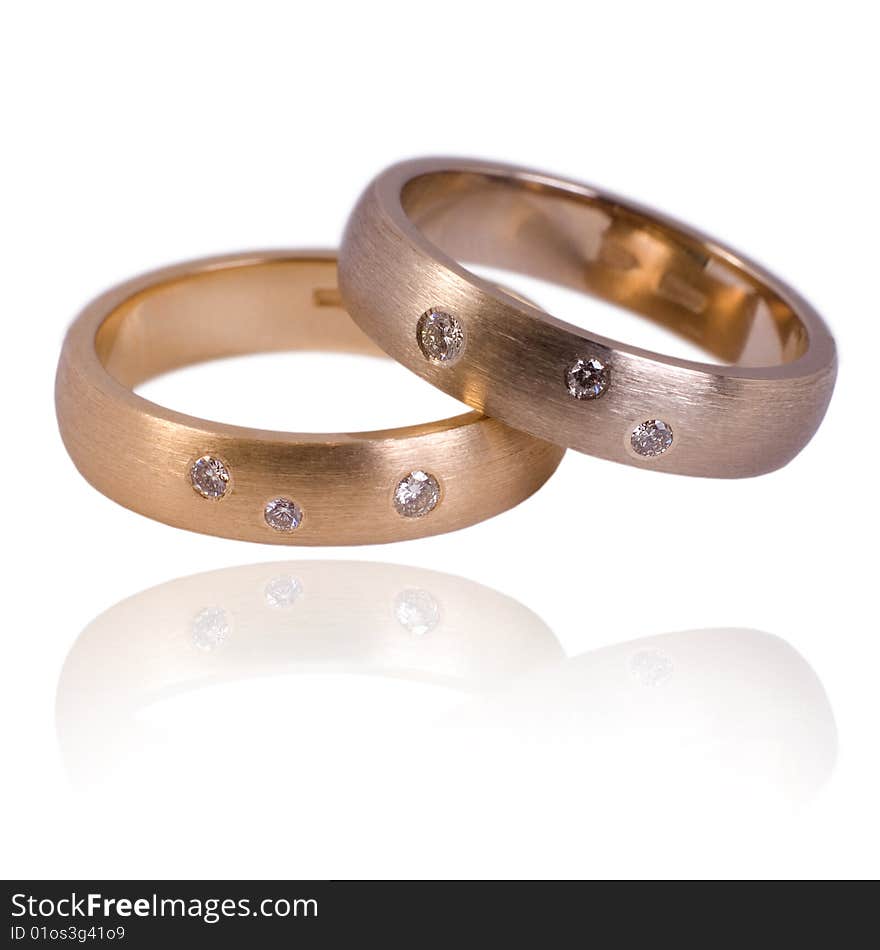 His and hers golden wedding bands, with diamonds. On a white background with soft reflection, isolated. His and hers golden wedding bands, with diamonds. On a white background with soft reflection, isolated.