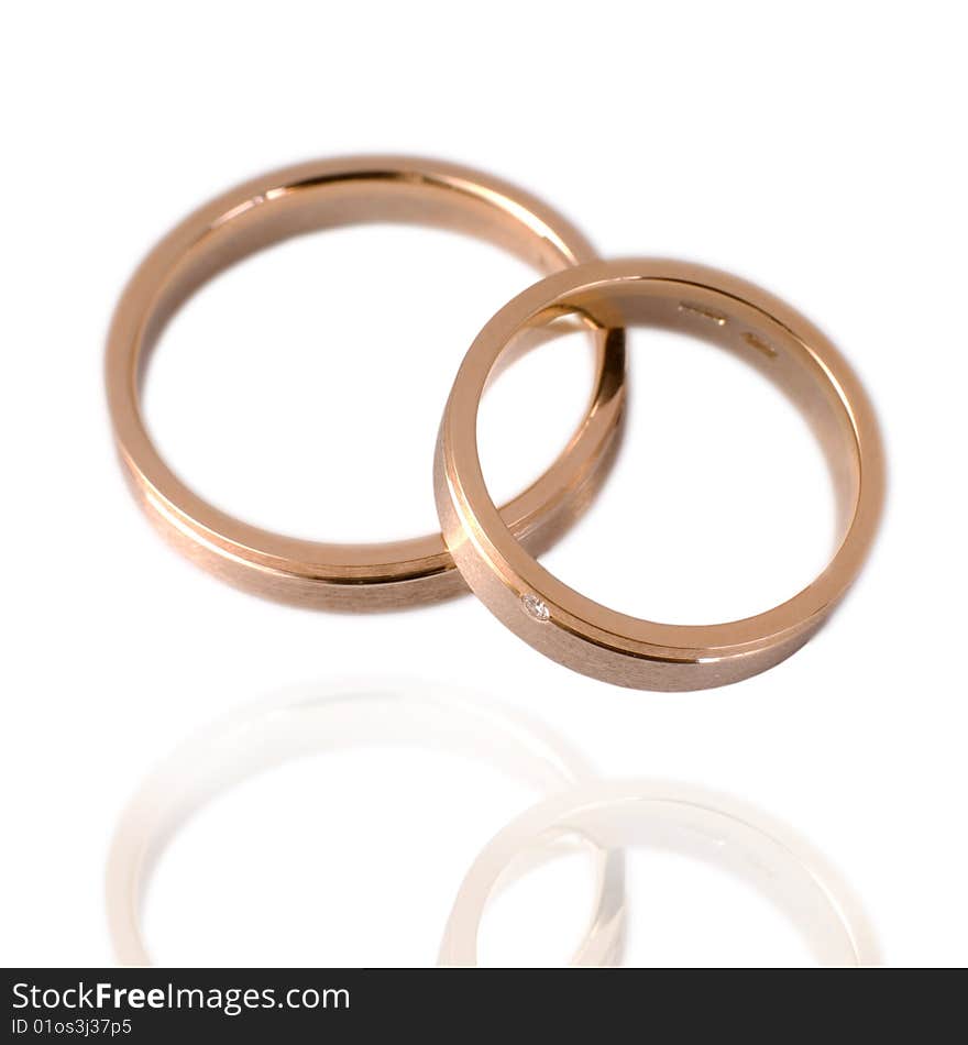 His and hers golden wedding bands, with diamonds. On a white background with soft reflection, isolated. His and hers golden wedding bands, with diamonds. On a white background with soft reflection, isolated.