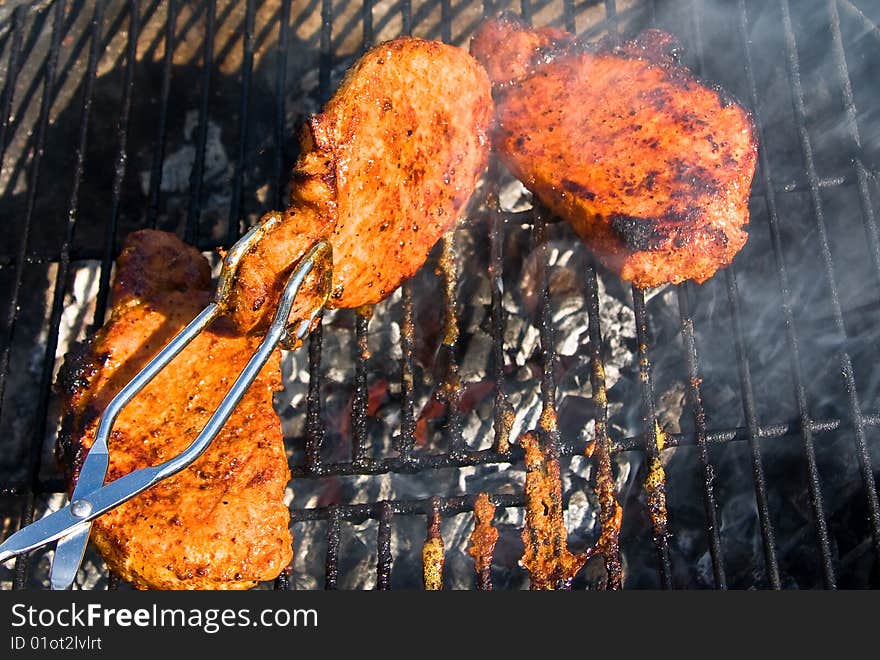 Pork shop being grilled and turned so it not will get burned. Pork shop being grilled and turned so it not will get burned