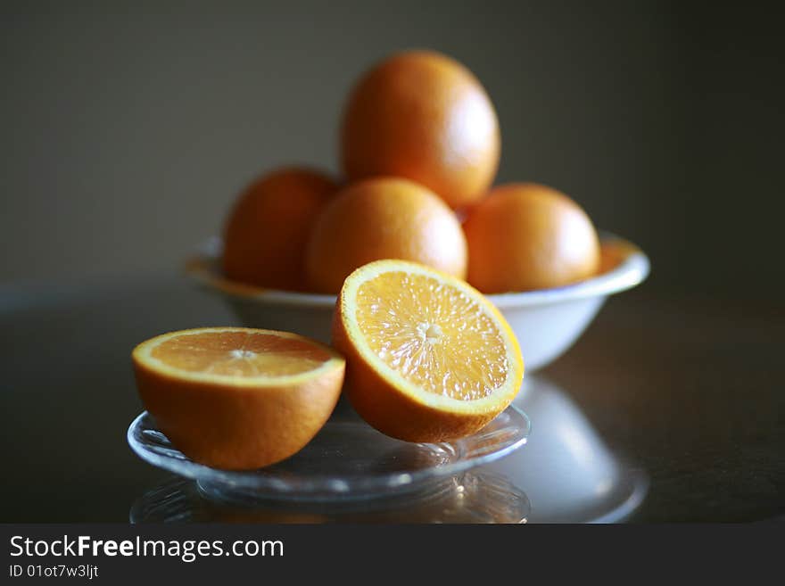 Sliced orange on a plate with bowl of oranges in background.