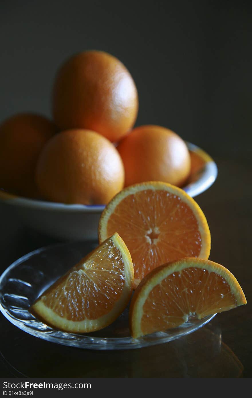 Sliced oranges on a plate with bowl of oranges in the background