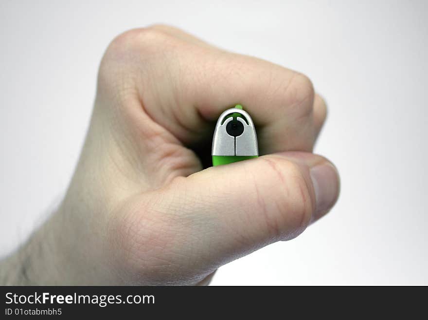 A hand/ fist holding a green and silver cigarette lighter, directing the gas nozzle towards the camera as in a top-down view, the hand pressing the trigger, against a white gradient background. A hand/ fist holding a green and silver cigarette lighter, directing the gas nozzle towards the camera as in a top-down view, the hand pressing the trigger, against a white gradient background