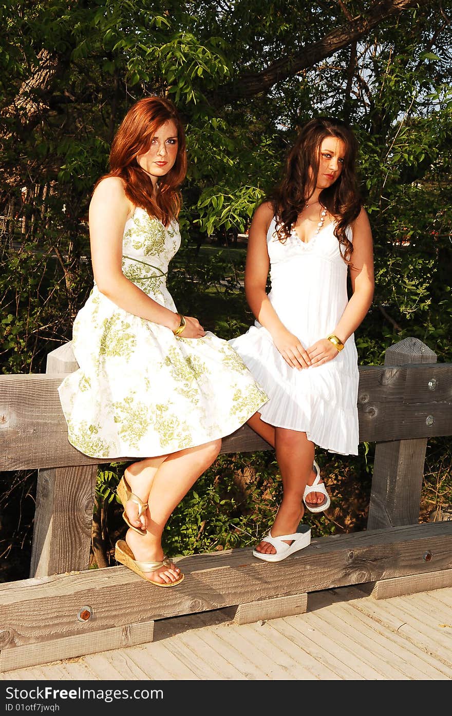 Two very pretty sisters sitting on the railing of a bridge in nice summer dresses, but looking quit sad. Two very pretty sisters sitting on the railing of a bridge in nice summer dresses, but looking quit sad.