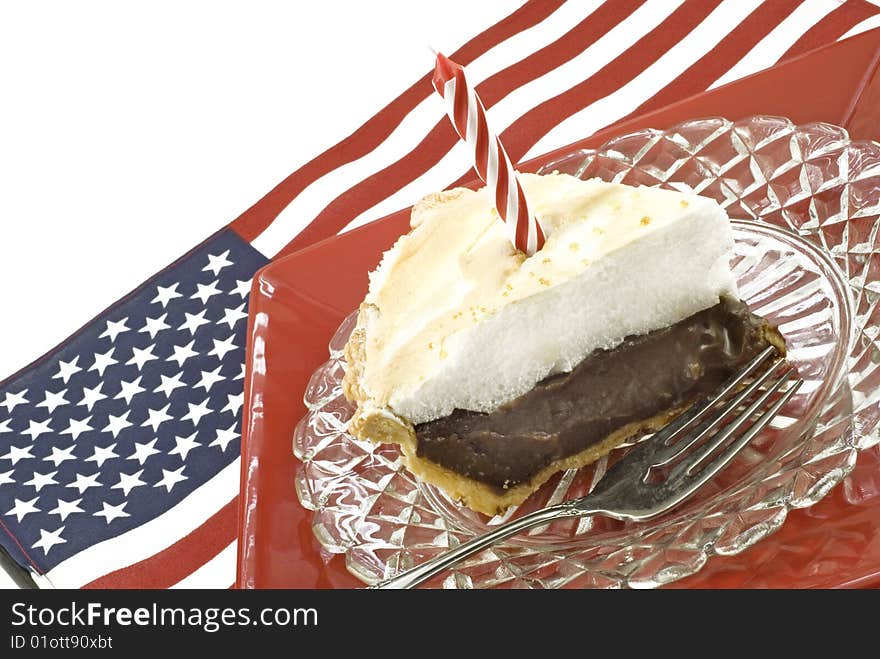 A pie of homemade chocolate meringue pie with one candle on an american flag background, horizontal with copy space. A pie of homemade chocolate meringue pie with one candle on an american flag background, horizontal with copy space