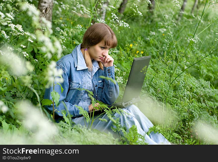 The beautiful girl with the laptop in park sits in a green grass. The beautiful girl with the laptop in park sits in a green grass