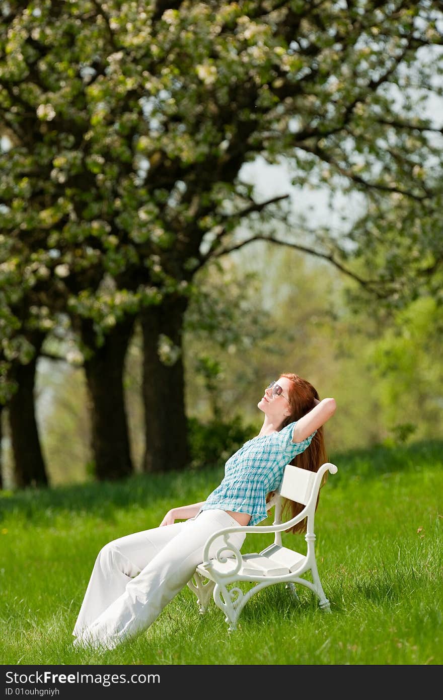 Red hair woman relaxing on white bench in summer meadow; shallow DOF. Red hair woman relaxing on white bench in summer meadow; shallow DOF