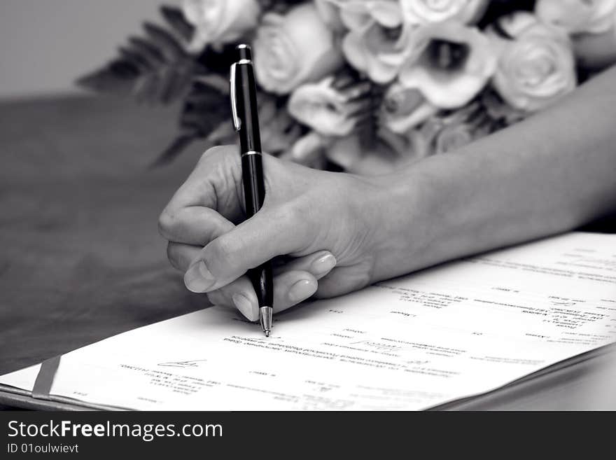 Woman's hand signing documents near a wedding bouquet. Woman's hand signing documents near a wedding bouquet