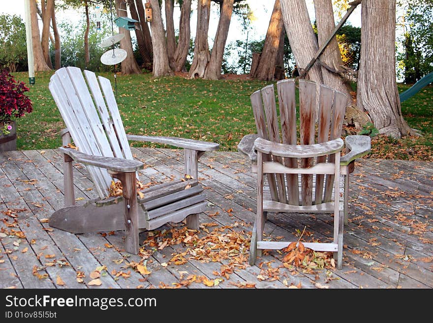 A fall setting with leaves blowing and winter about to set in. Two Muskoka Chairs left out on a deck at the cottage. A fall setting with leaves blowing and winter about to set in. Two Muskoka Chairs left out on a deck at the cottage