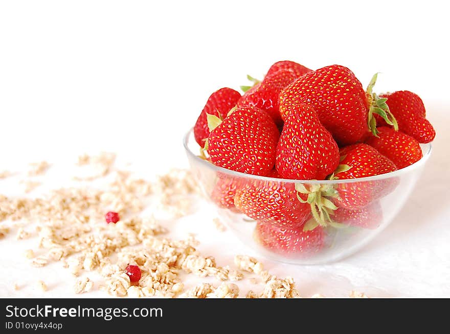 Strawberries in a glass bowl and muessli on a white table. Strawberries in a glass bowl and muessli on a white table