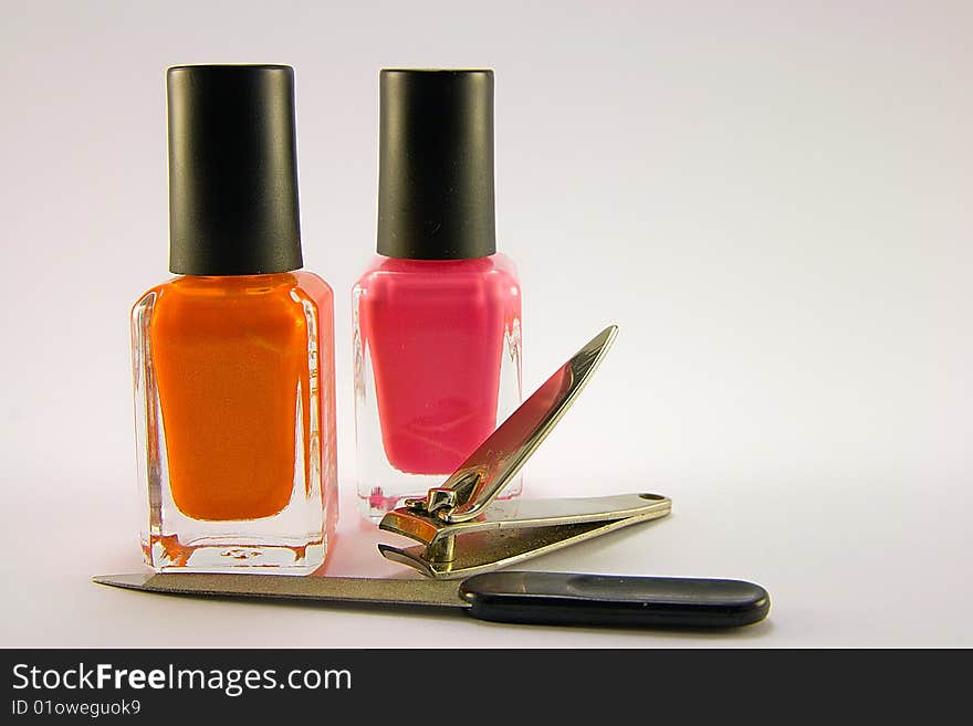 Orange and pink nail polish with nail file and clippers on a plain background. Orange and pink nail polish with nail file and clippers on a plain background