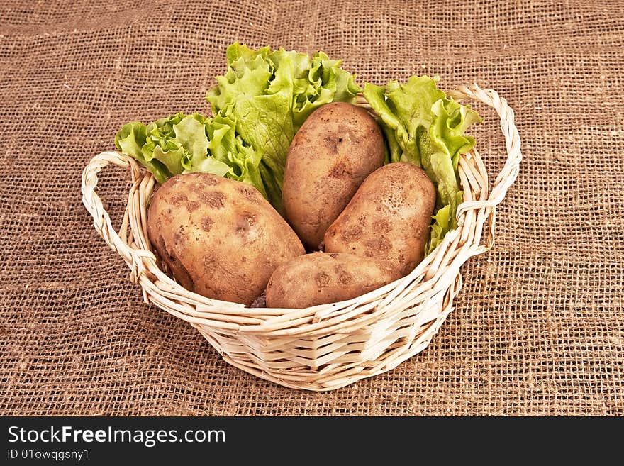 Four raw potatoes and lettuce in basket on rough linen fabric. Four raw potatoes and lettuce in basket on rough linen fabric.