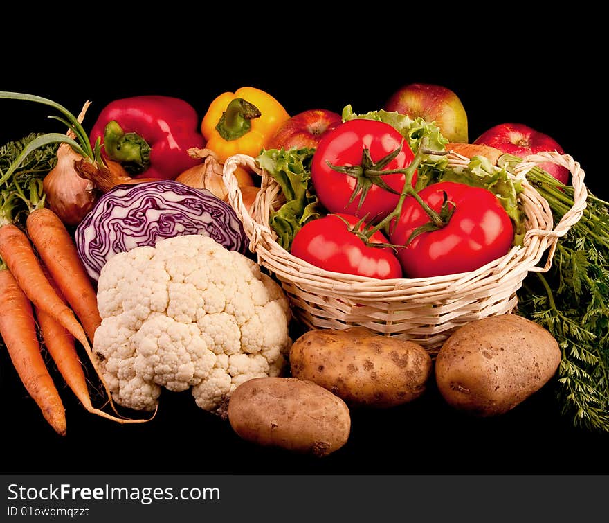 Pile of various vegetables. Isolated on black. Three tomatoes in basket, carrots, paprika, potatoes, onions.