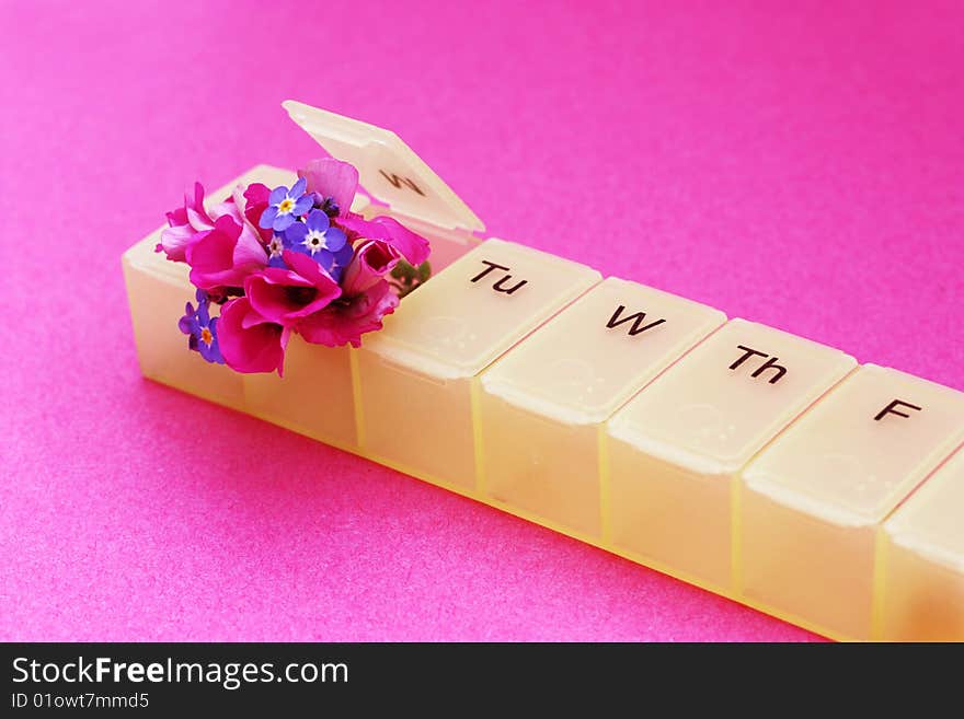 A seven day pill dispenser with small fresh flowers popping out of it. A seven day pill dispenser with small fresh flowers popping out of it