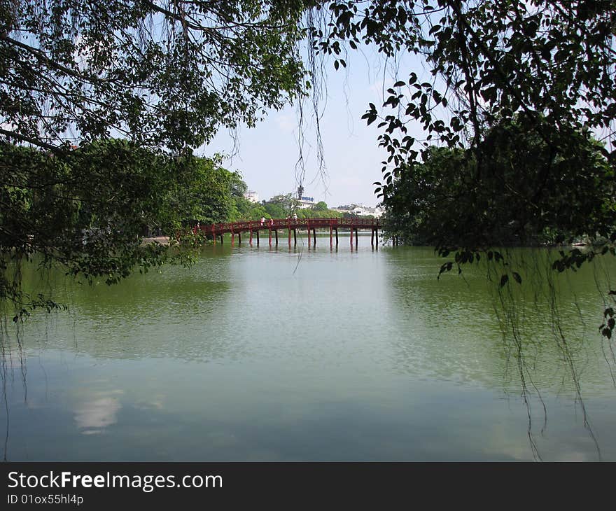 Photo of a red bridge that crosses part of a lake in central hanoi to an island with a pagoda that overlooks the lake.