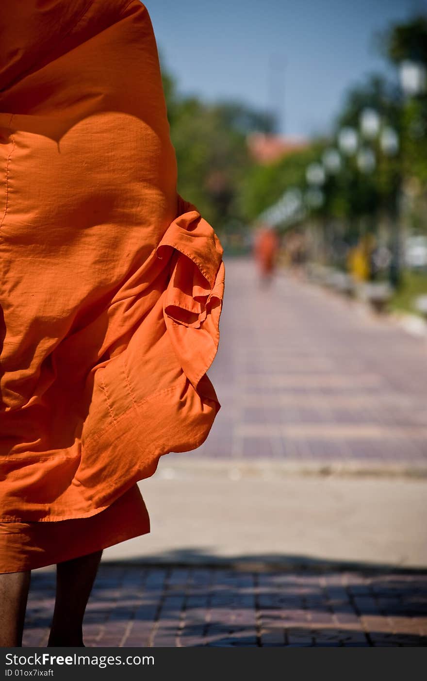 A monk walks the streets in asia, the wind blowing his loosely fitting robe. the vibrant orange color stands out nicely in the urban setting. shadow of his umbrella can be seen on his shoulders showing that he is keeping cool under the hot asian sun. A monk walks the streets in asia, the wind blowing his loosely fitting robe. the vibrant orange color stands out nicely in the urban setting. shadow of his umbrella can be seen on his shoulders showing that he is keeping cool under the hot asian sun.