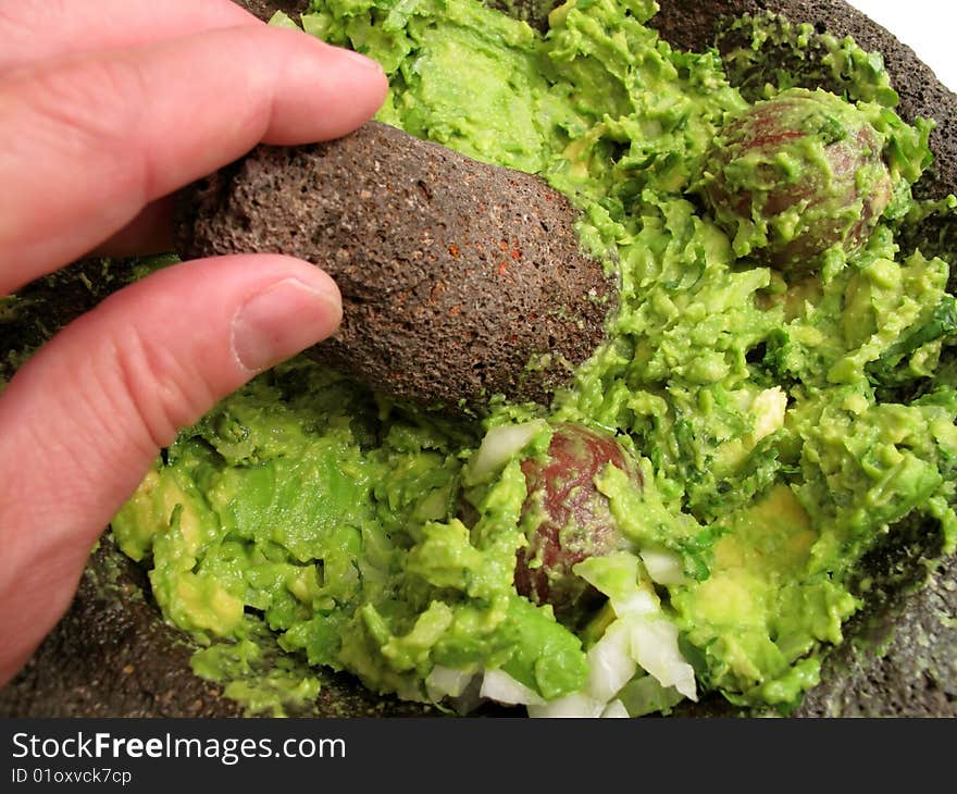 Photo of guacamole being prepared using a traditional cooking instrument known as a molcajete.  Guacamole is made by combining avocado, cilantro and onions then mashing into a paste. Photo of guacamole being prepared using a traditional cooking instrument known as a molcajete.  Guacamole is made by combining avocado, cilantro and onions then mashing into a paste.